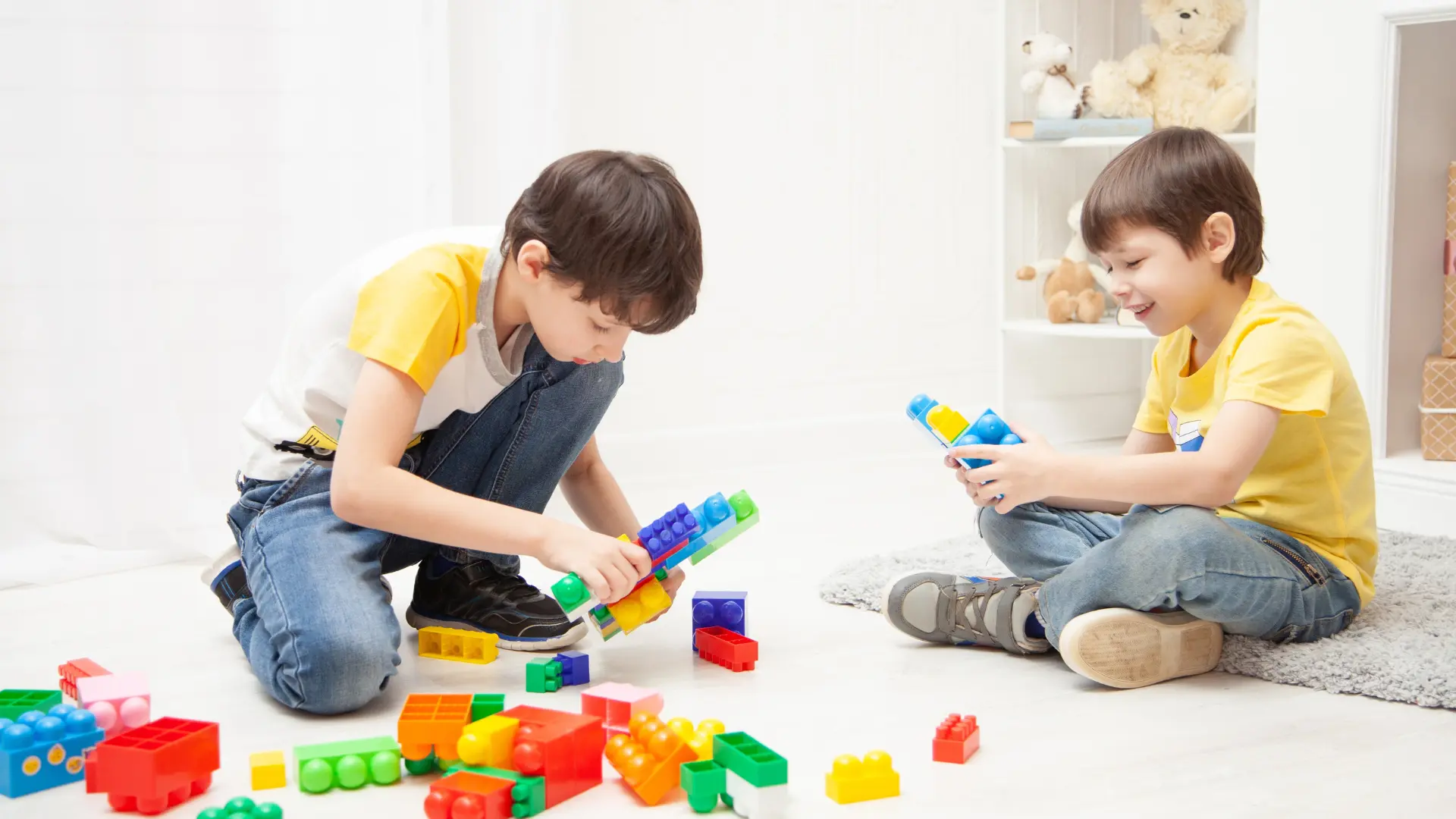 Two boys engaged in play, building structures with colorful toy blocks on the floor, promoting emotional regulation skills.
