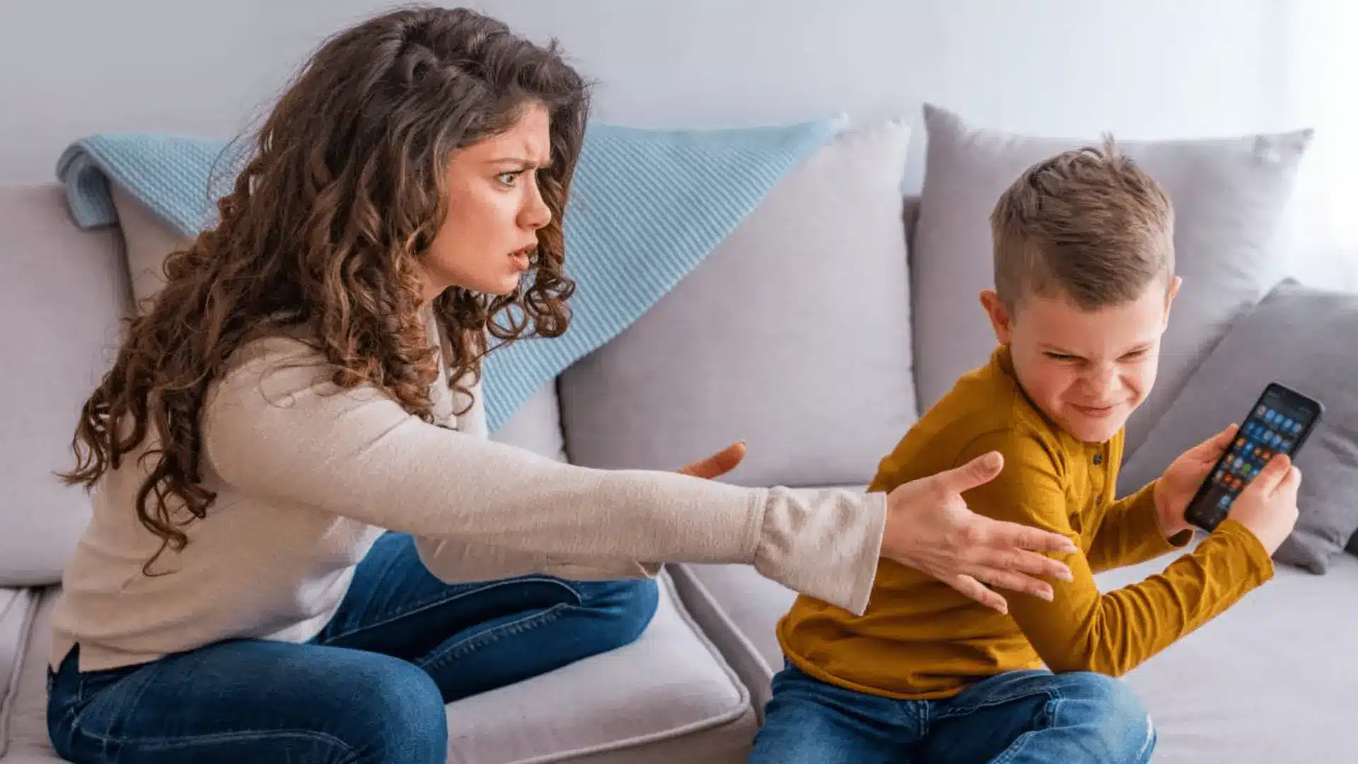 Mother reaching to take a smartphone from her son as he turns away, showing tension over screen time limits at home.
