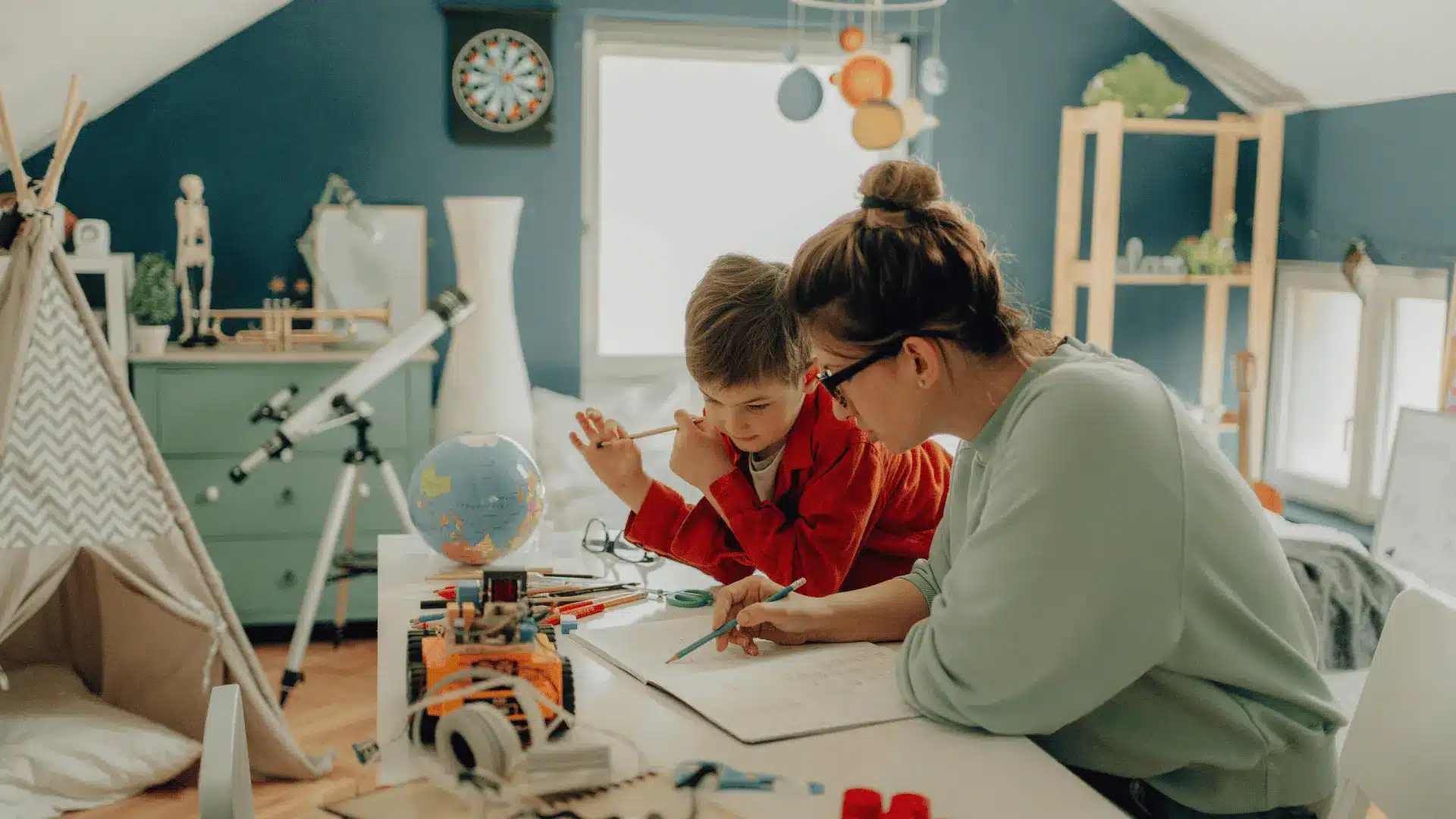 A woman and a child engage in a hands-on art project together in a well-lit room, surrounded by various art supplies.