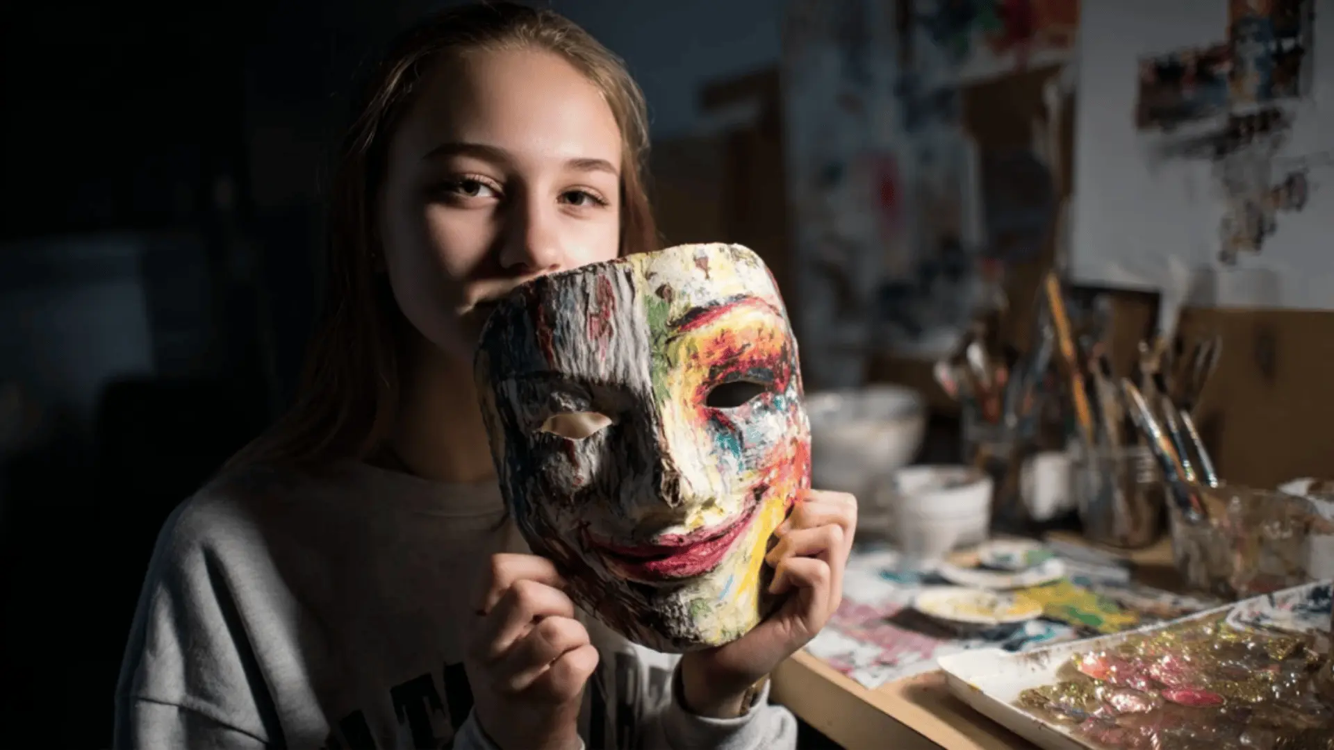 a teen holding a half-bright, half-dark emotion mask