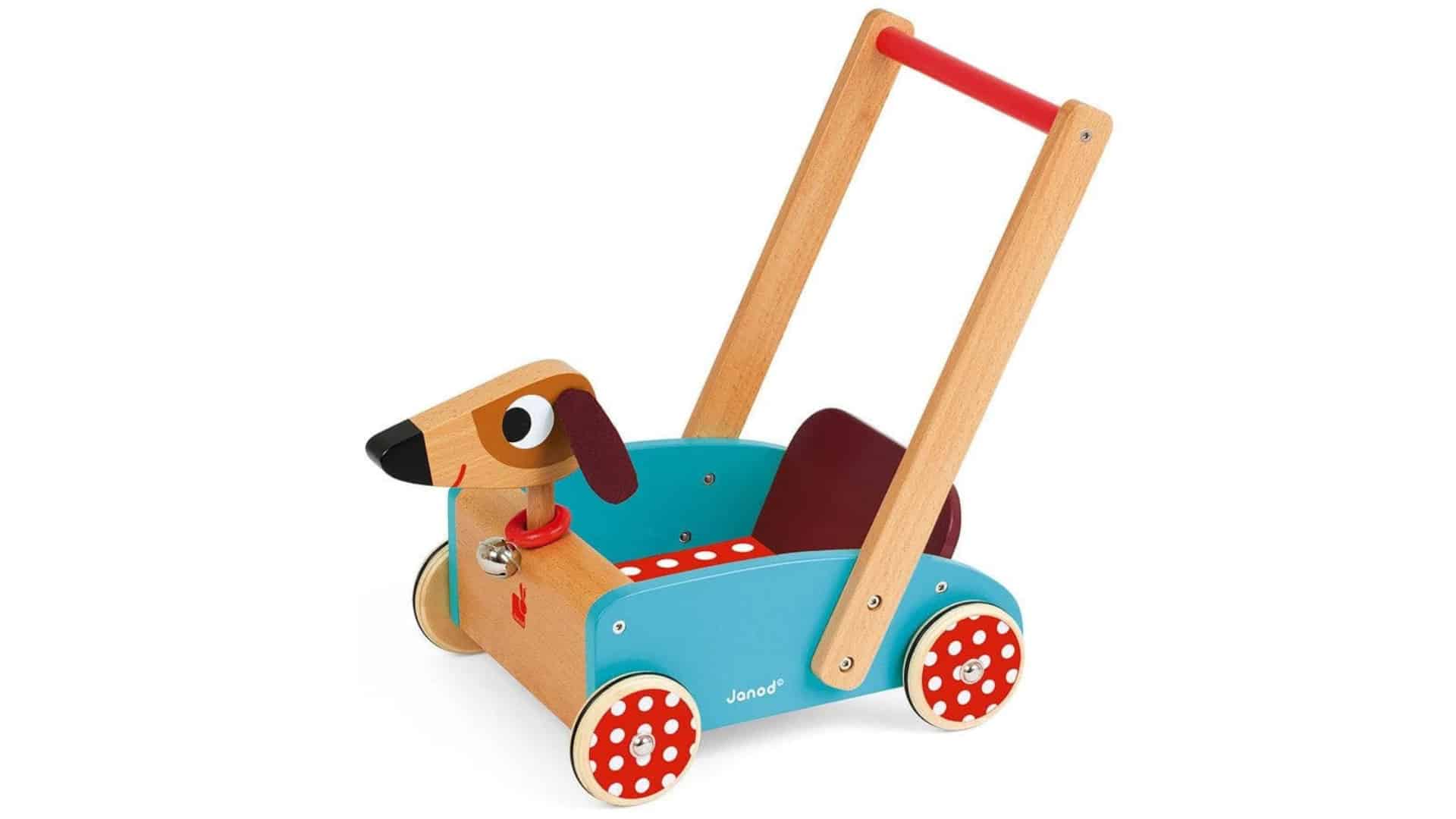 Wooden dog push walker cart with red handle, blue body, and red polka dot wheels, isolated on white background