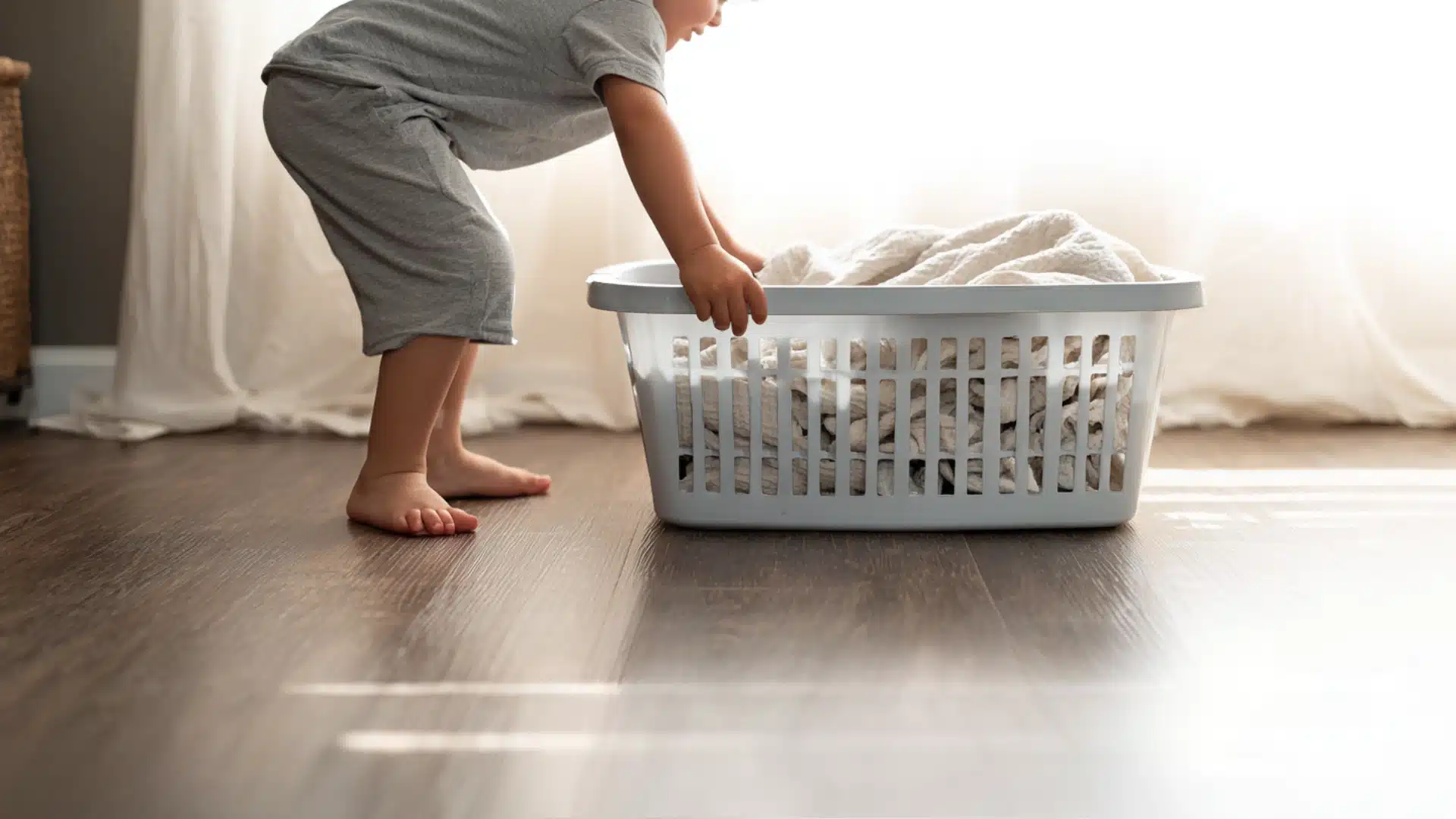 Toddler pushing a laundry basket across the floor during a push-and-pull game to build coordination and body control.