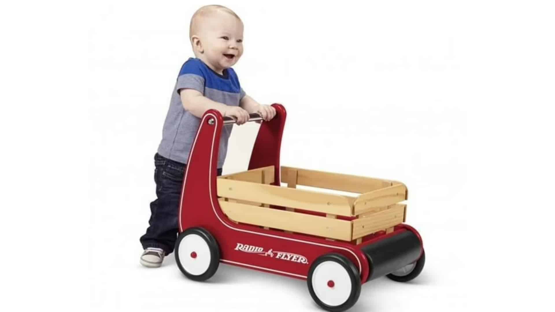 Red Radio Flyer classic walker wagon with wood crate and black bumper, shown with a toddler pushing in a studio photo
