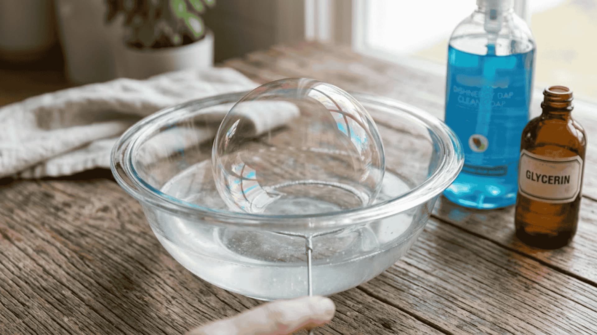 Close-up of a bubble forming over a glass bowl with dish soap and glycerin on a wooden table.