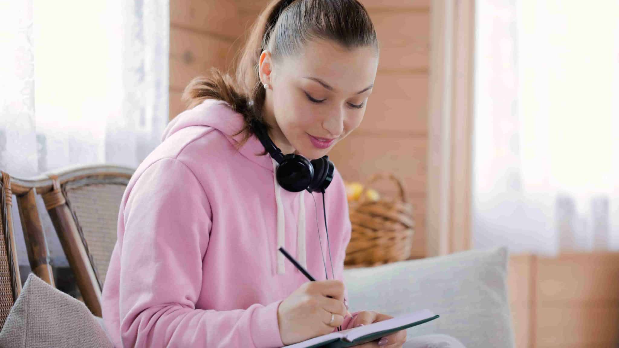 a girl writing on diary with headphones resting on the neck